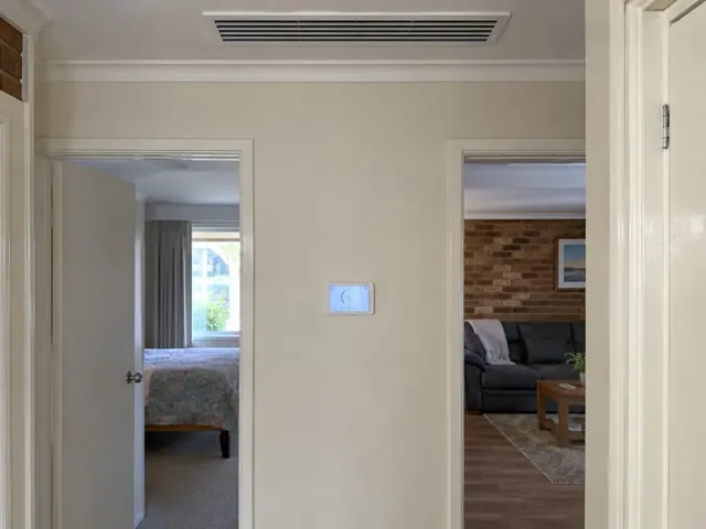 Hallway with a ceiling ducted air vent and wall controller in a home interior in Andrews Farm