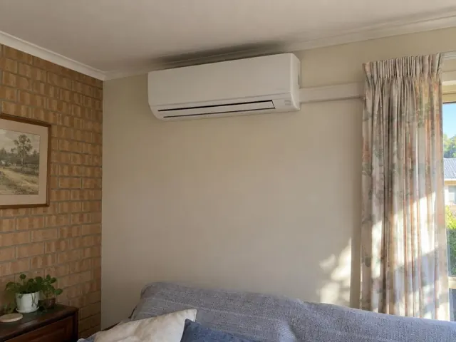 Wall-mounted split system above a lounge sofa beside a brick feature wall and curtain in Craigmore